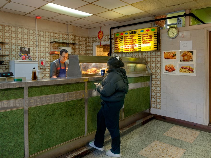 A photograph of a girl waiting at the counter of a fish bar with a man serving her