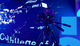 Professional video camera on tripod filming in front of a vibrant digital screen with abstract text and graphics.