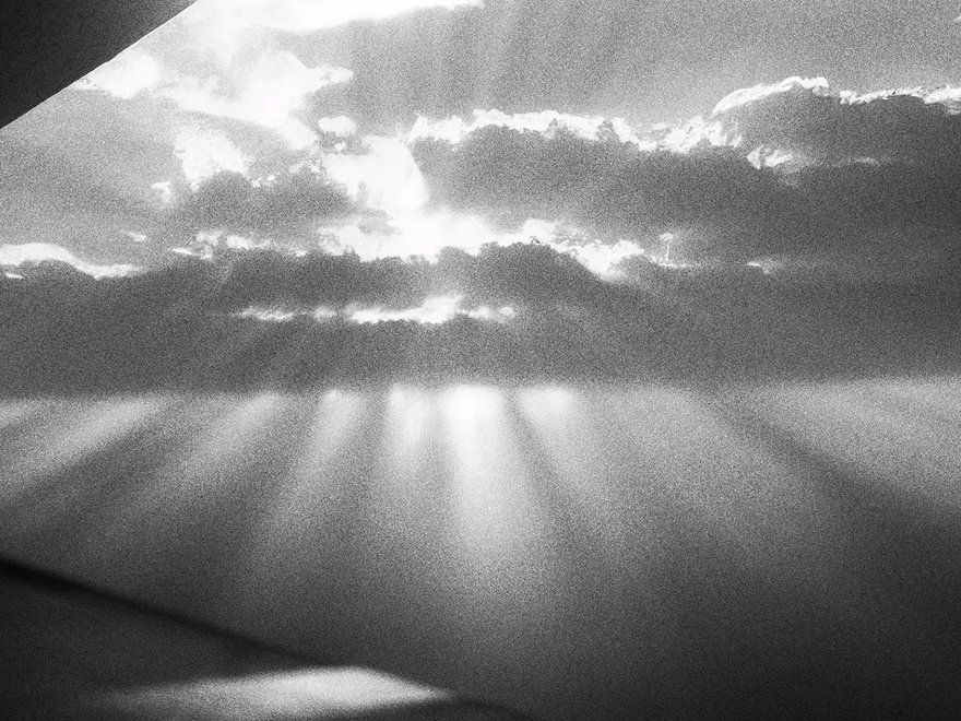 grainy black and white photograph of the sun breaking through clouds